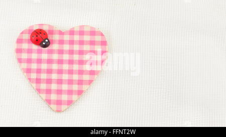 Pink plaid cuore con una coccinella su sfondo bianco Foto Stock