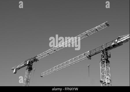 Immagine in bianco e nero di torre due gru edili rivolte in direzioni opposte contro un cielo chiaro Foto Stock