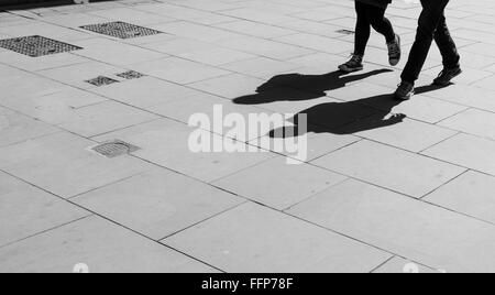 Le ombre dei due pedoni a piedi proiettata sul marciapiede. in bianco e nero. Foto Stock