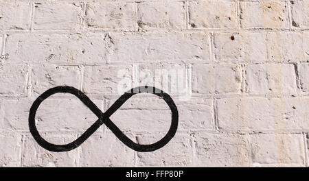 Il simbolo di infinito disegnato in nero su un muro di mattoni dipinto in bianco. Foto Stock