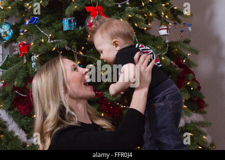 Madre e figlio avente un momento di divertimento nella parte anteriore della scena di Natale con albero e decorazioni in background. Foto Stock