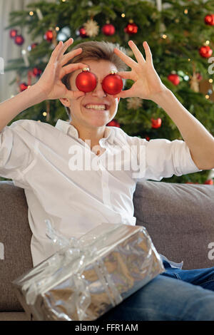 Il giovane adolescente con red baubles davanti agli occhi, Natale, Germania Foto Stock