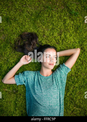 Bella giovane donna giace sul muschio verde rilassante con le mani dietro la sua testa sorridente Foto Stock