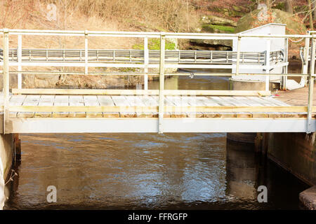 Un piccolo ponte che attraversa oltre la piccola diga idroelettrica in Djupafors, Svezia. Foto Stock