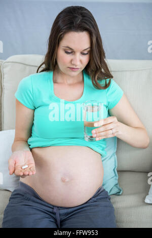 Donna incinta tenendo un bicchiere di acqua e pillole Foto Stock