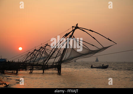 Cinese di reti da pesca a tarda sera colorato caldo cielo rossastro sole che tramonta dietro alla net , Fort Kochi Ernakulum Kerala Foto Stock