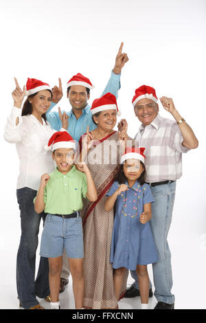 Il genitore di bambini con nonno indossa Babbo Natale caps alzando le mani con il dito indice rivolto verso l'alto Foto Stock