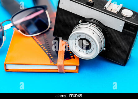 Vecchia fotocamera retrò,la striscia del film,occhiali da sole e album di foto su sfondo blu Foto Stock