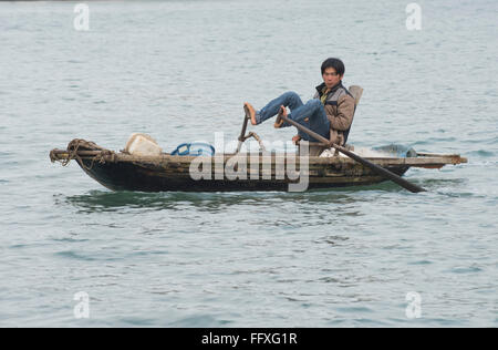 Una piccola barca a remi utilizzati per la pesca e i trasporti, uomo tradizionalmente utilizzando i suoi piedi alla fila di Halong Bay, Vietnam Foto Stock