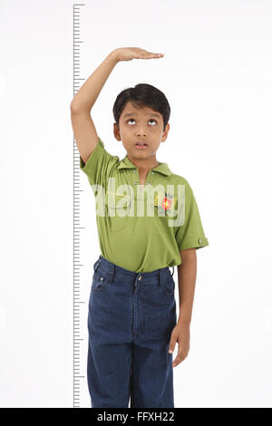 Dieci anni di vecchio ragazzo tenendo la sua mano sopra la sua testa per controllare la sua altezza signor#703V Foto Stock