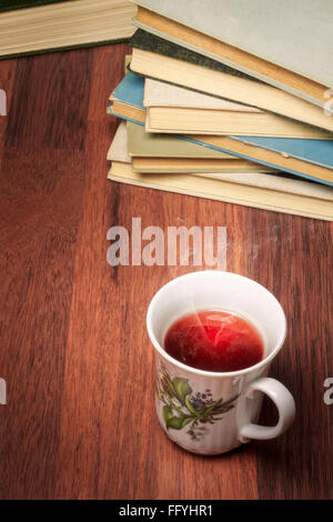 Tazza di tè in piedi accanto alla pila di libri antichi Foto Stock