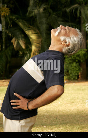 Anziano gentiluomo in blu scuro T shirt oltre sessanta anni di età facendo esercizi del mattino dalla piegatura all'indietro Foto Stock