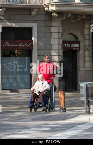 Il vecchio donna seduta su una sedia a rotelle con il suo caregiver camminando per le strade di Barcellona, in Catalogna, Spagna Foto Stock
