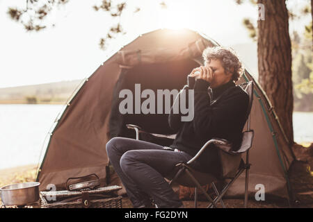 Ritratto di donna matura seduto nella sedia al campeggio di bere il caffè. La donna caucasica camping in natura sul giorno di estate. Foto Stock