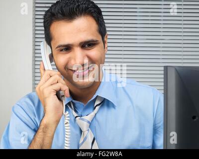 Il Multitasking executive parlando al telefono guardare il computer signor#779K Foto Stock