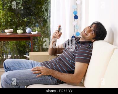 Giovane uomo ascoltare musica sulle cuffie in appoggio sul divano signor#702V Foto Stock