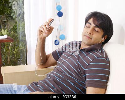 Giovane uomo chiuso gli occhi ascoltando la musica sulle cuffie in appoggio sul divano signor#702V Foto Stock