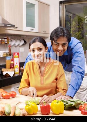 Giovane uomo in piedi dietro la donna per affettare il cetriolo sul tagliere signor#702V,702U Foto Stock