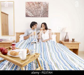 Giovane uomo e donna di bere succo di frutta aventi la prima colazione sul letto signor#702V,702U Foto Stock