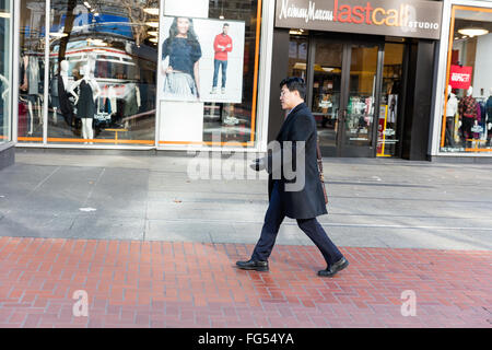 Uomo adulto di un etnia asiatica che indossa un mantello nero a camminare su un marciapiede Foto Stock