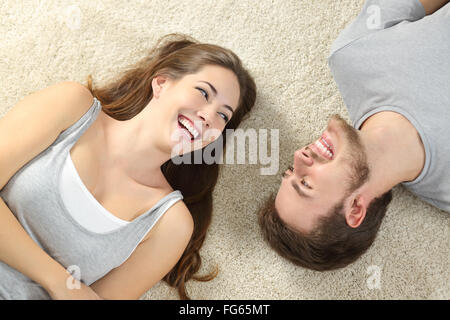 Coppia felice ridere cercando fra loro e giacenti su un tappeto a casa Foto Stock