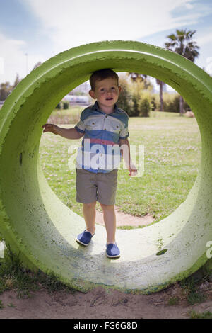 Ritratto di un bambino ragazzo nasconde al suo interno l'anello di calcestruzzo e giocare nel parco durante il giorno d'estate. Foto Stock