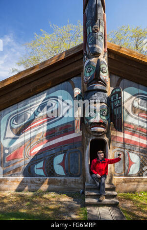 Uomo si siede sui gradini di un clan Tlingit house con smart phone, Totem Bight stato storico Park, Ketchikan, a sud-est di Alaska, STATI UNITI D'AMERICA, molla Foto Stock