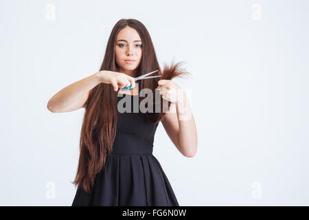 Fiducioso grave giovane donna in piedi e tagliare le estremità di sdoppiamento dei suoi lunghi capelli fragili su sfondo bianco Foto Stock