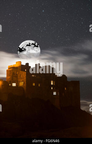 Santa nella sua slitta e renne profilarsi nel cielo stellato di fronte la luna su edifici; Bamburgh, Northumberland, Inghilterra Foto Stock