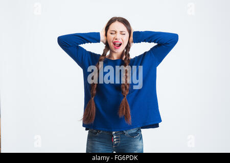 Sottolineato frustrato giovane donna con due lunghe trecce coperto le orecchie con le mani e urlando Foto Stock