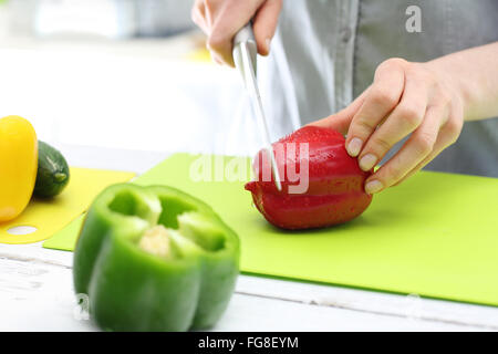 La donna taglia pepe per insalata. Donna mani mentre i peperoni di taglio sul bancone della cucina. Foto Stock