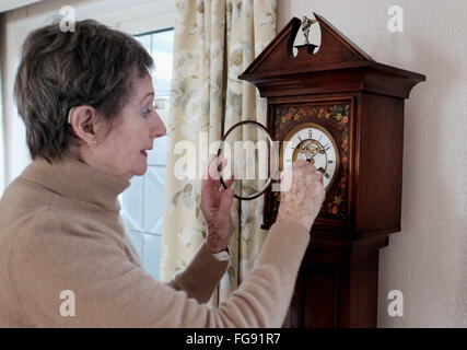 Signora anziana che avvolge la sua nipote antica orologio nella sua sala da pranzo a casa mettendo tempo avanti o indietro Foto Stock