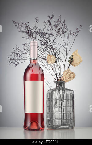 Vino rosato bottiglia con etichetta mockup per appassiti rose bianche in un vaso. Foto Stock