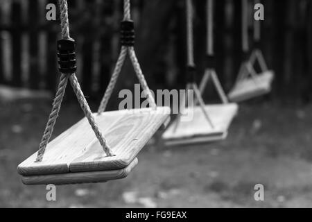 Posizione orizzontale in prospettiva di tre di legno altalene per bambini nel parco con profondità di campo Foto Stock