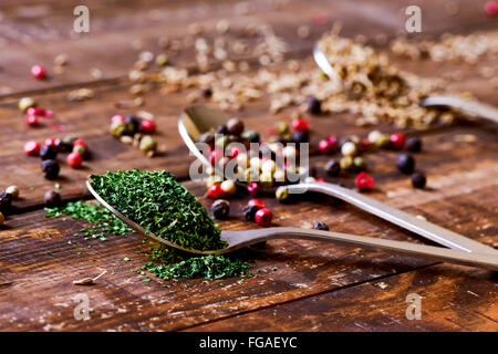 Tre cucchiai colmi di trito di prezzemolo essiccato, grani di pepe di diverse varietà e i semi di anice su una tavola in legno rustico Foto Stock