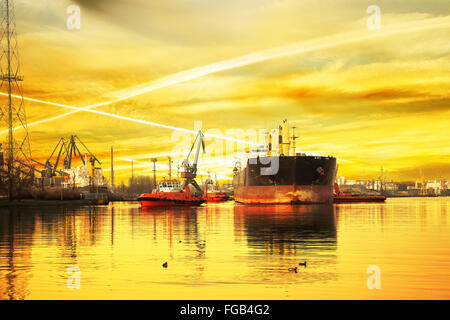 Grande nave con la scorta rimorchiatori partenza dal porto al tramonto. Foto Stock