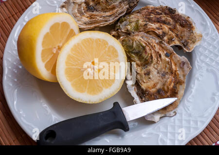 Preparazione dei molluschi destinati al consumo,aprirlo, sullo sfondo di limone in una mano d'uomo Foto Stock