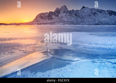 A frozen fjord on the Lofoten in northern Norway with the low midday sun behind the mountains. Foto Stock