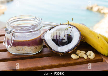 Cherry banana di noce di cocco per tutta la notte di avena con crepe aperte coco, banana, anacardi mescolati con semi di Chia e crema di ciliegio in un mason j Foto Stock