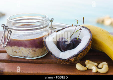 Cherry banana di noce di cocco per tutta la notte di avena con crepe aperte coco, banana, anacardi mescolati con semi di Chia e crema di ciliegio in un mason j Foto Stock