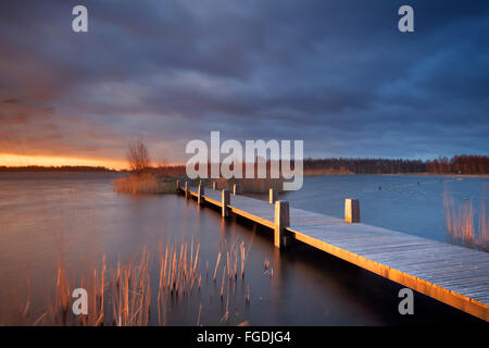 Una passerella su un lago con un cielo minaccioso. Fotografato a sunrise. Foto Stock