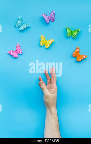 Una mano protesa alla cattura un gruppo di farfalle variopinte o blu brillante background. Foto Stock