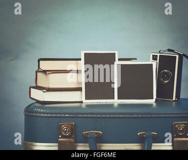 Le vecchie fotografie, una fotocamera e libri sono sulla parte superiore di una valigia vintage con uno sfondo blu per un concetto di memoria Foto Stock