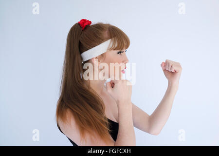 Donna con capelli lunghi marrone che indossa una Fascia assorbisudore di testa con i suoi pugni rinserrata preparando ad impegnarsi nella boxe Foto Stock