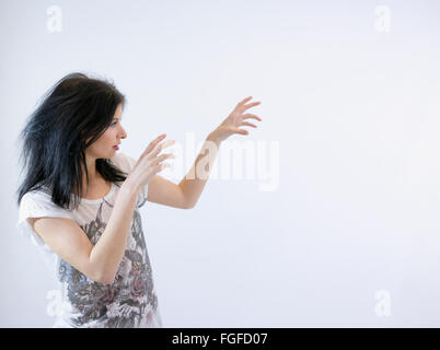 Donna con lunghi capelli neri prestidigitazione magia con le mani in aria Foto Stock