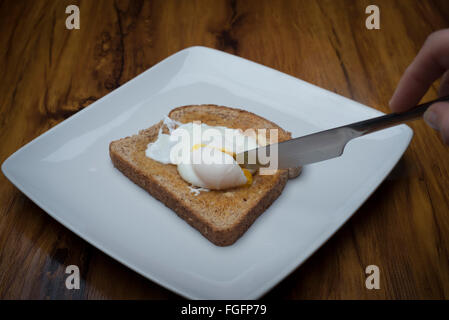 Una lama di taglio in un uovo in camicia su toast Foto Stock