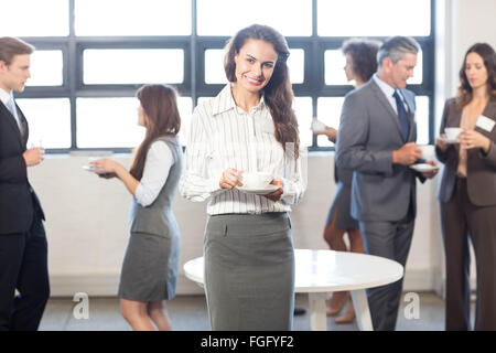 Imprenditrice sorridente alla telecamera mentre i suoi colleghi in piedi in background Foto Stock