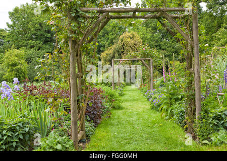 Vegetali e Flower Garden cottage con un erba verde percorso a piedi in legno arco di rose Foto Stock