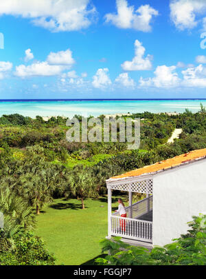 Donna in piedi su una veranda che si affaccia sull'oceano a Parrot Cay Resort , Turks e Caicos. Foto Stock