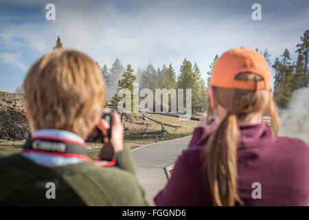 Due donne a scattare foto di bison vagare attraverso un campo di geyser. Foto Stock